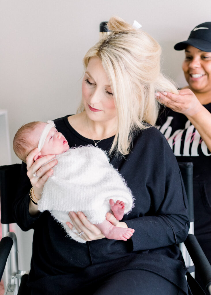 Mom in her pajamas getting hair done by hair and makeup artist in brandon, mississippi studio before newborn photography session while holding newborn. 