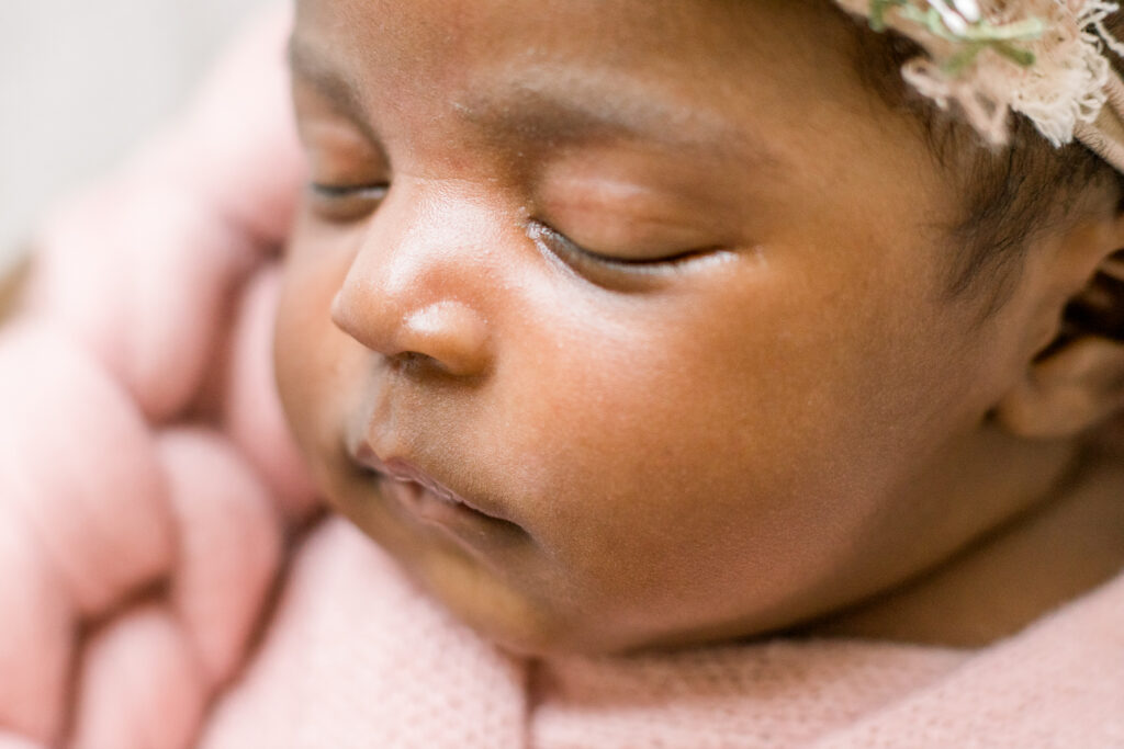 Close up on newborn baby girl's face, swaddled in pink fabric in wooden bowl by Mississippi Newborn Photographer.