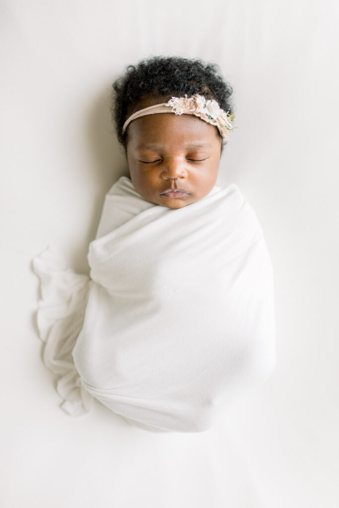 Newborn baby girl in studio swaddled in white fabric on bean bag by Mississippi Newborn Photographer.