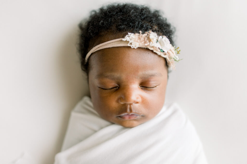 Newborn baby girl swaddled in white fabric on white bean bag by Mississippi Newborn Photographer.