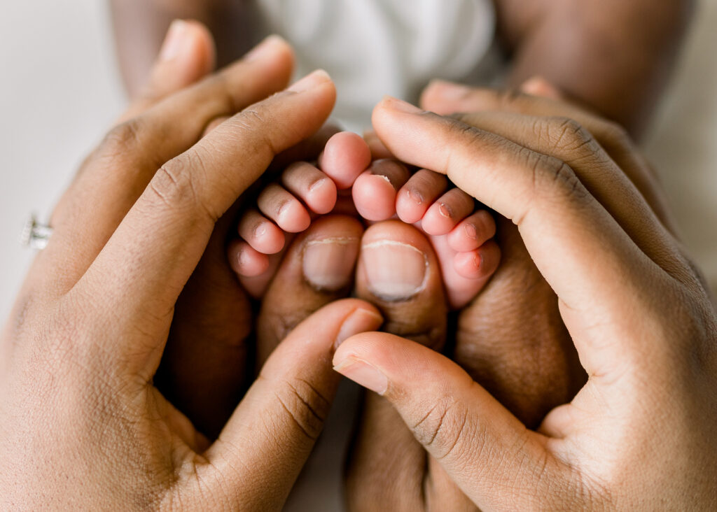 Newborn baby girl in studio with close up on mom and dad's hands around baby's toes by Mississippi Newborn photographer. 