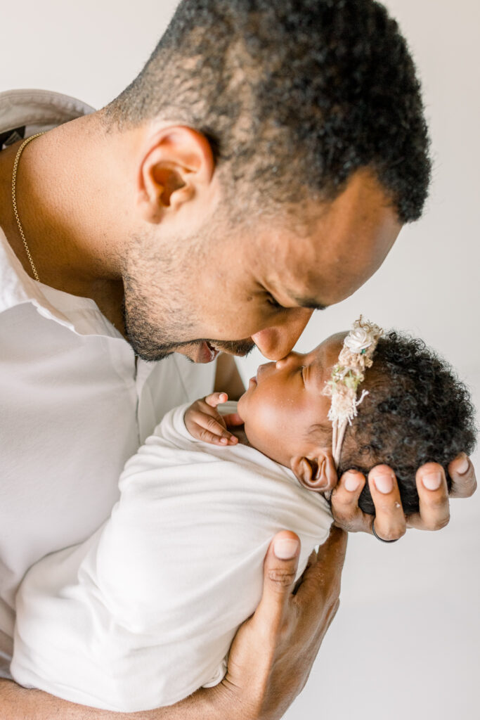 Newborn baby girl session in white studio with dad holding baby and rubbing noses with baby. Image by Mississippi Newborn Photographer. 