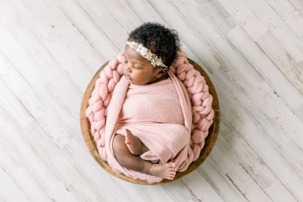 Newborn baby girl in pink swaddle in wooden bowl in studio by Mississippi Newborn Photographer.