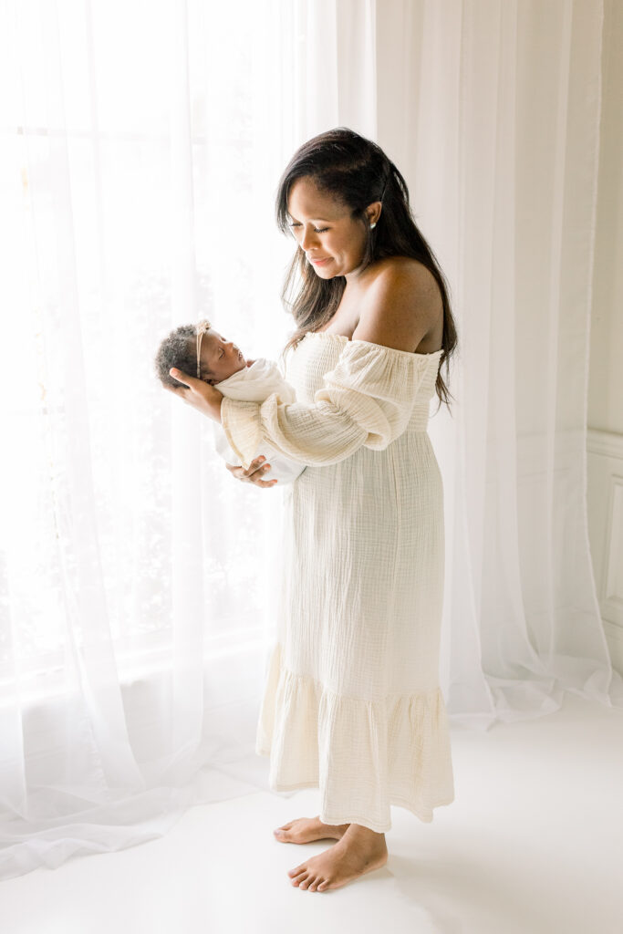 Mississippi newborn photographer captures mom holding newborn baby girl swaddled in white in white natural light studio. 