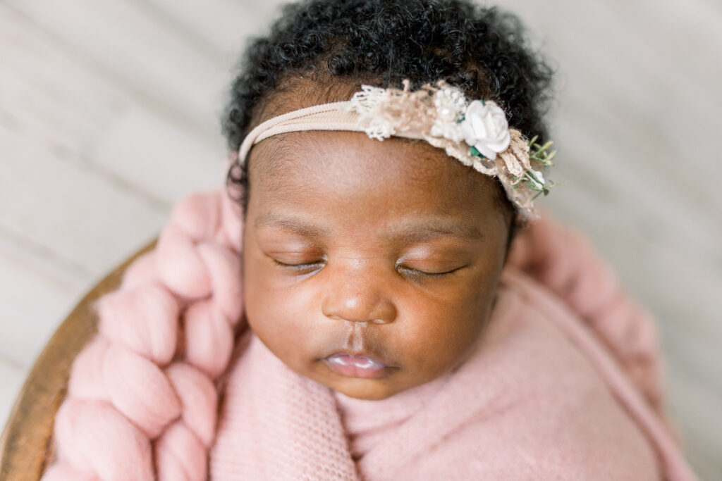 Newborn baby girl swaddled in pink fabric in wooden bowl by Mississippi Newborn Photographer.