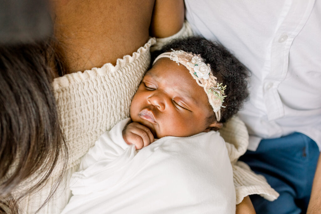 Close up on newborn baby girl swaddled in white while being held by mom and dad. Image captured by Mississippi Newborn Photographer. 