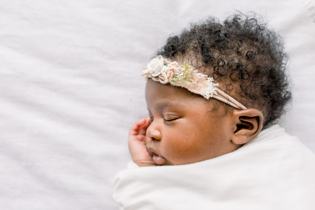 Close up of newborn baby girl swaddled n white on white bed in natural light studio by Mississippi newborn Photographer.