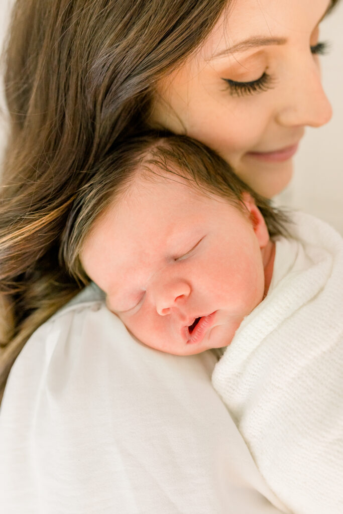 Mom dressed in white snuggling newborn baby boy. Image taken by CJ and Olive photography a Madison, MS Newborn Photographer. 