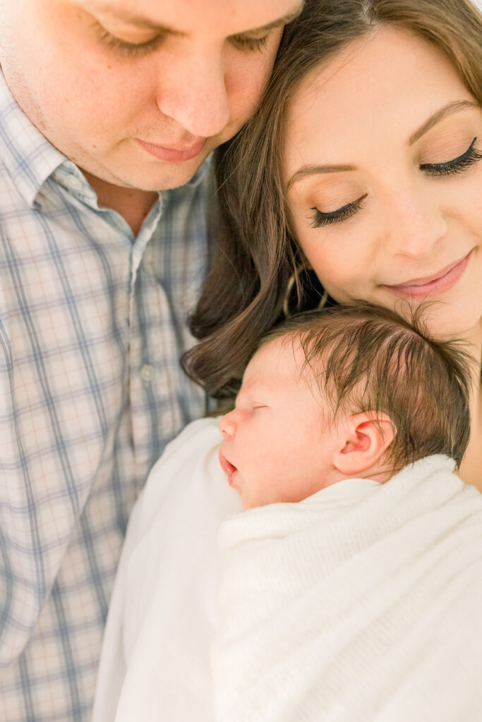 Mom and dad snuggling close together looking down at newborn baby boy on mom's shoulder. Image captured by Madison, MS Newborn Photographer.