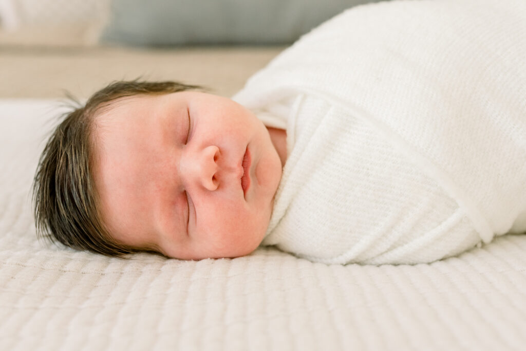 Close up on newborn baby boy swaddled in white laying on neutral bedding. Image taken by Madison, MS newborn photographer.