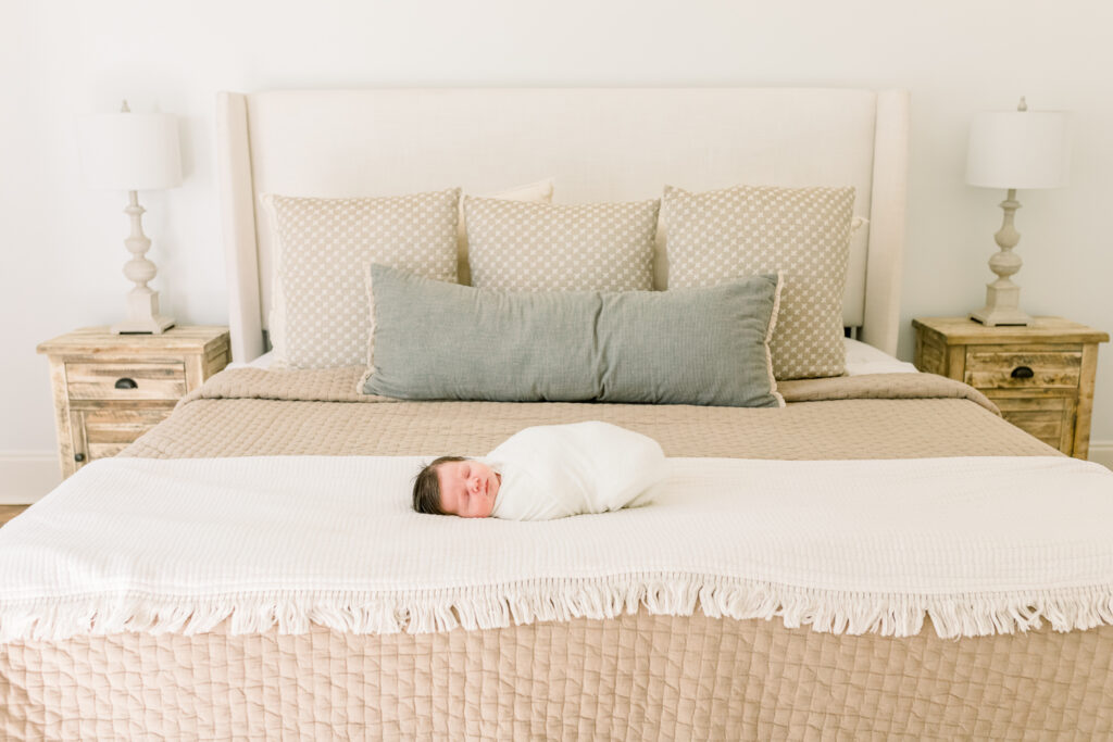 Newborn baby boy swaddled in white laying on neutral bedding. Image taken by Madison, MS newborn photographer.