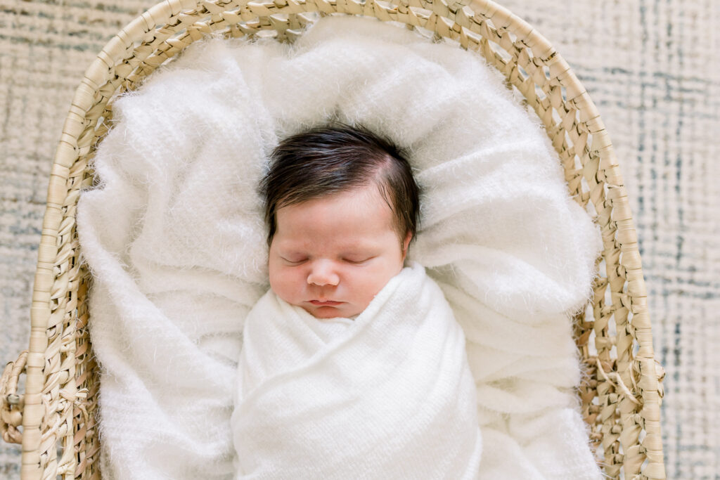 Newborn baby boy swaddled in white in moses basket with white blankets. Image captured by CJ and Olive photography, a Madison, MS photographer.