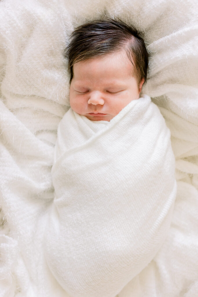 Newborn baby boy swaddled in white in moses basket with white blankets. Image captured by CJ and Olive photography, a Madison, MS photographer.