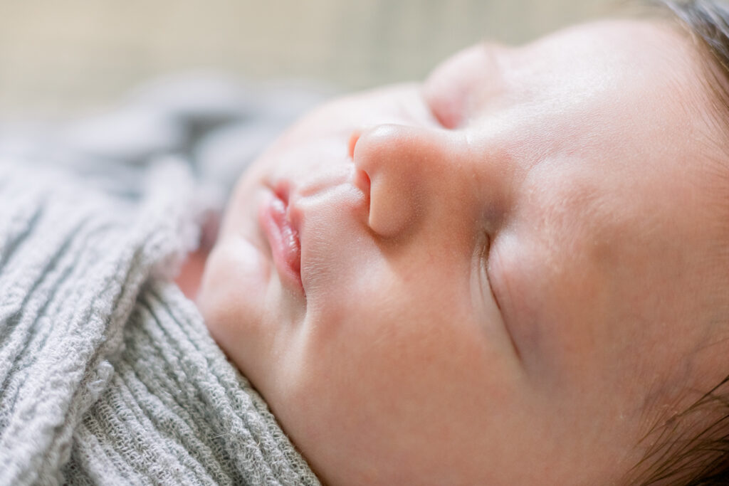 Profile shot of newborn baby boy swaddled in grey in wooden bowl with grey stuffing. Image captured by Madison, MS newborn photographer, CJ and Olive Photography.