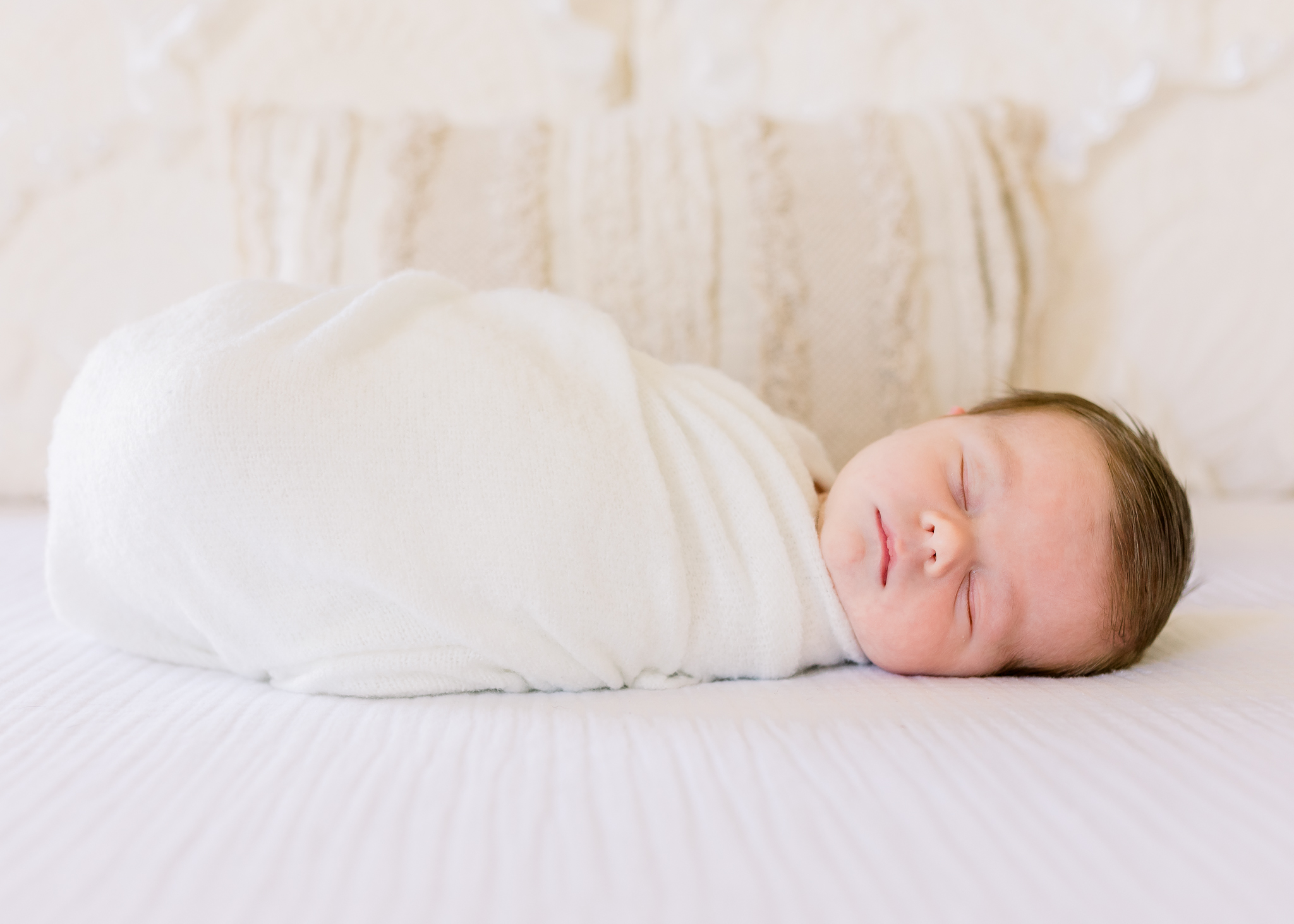 Madison newborn photographer captures image of baby boy swaddled in white fabric on white linen bedding.