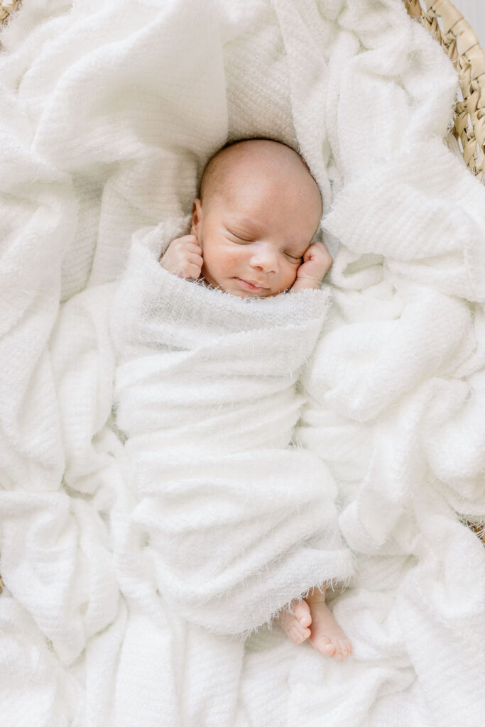 Newborn baby boy swaddled in white in Moses basket in white studio by CJ and Olive Photography, a Brandon newborn photographer. 