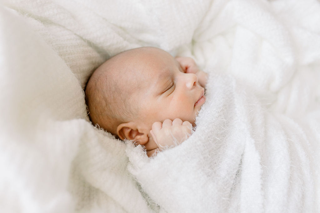 Profile image of newborn baby boy swaddled in white in Moses basket in newborn studio. Image take by CJ and Olive Photography. 