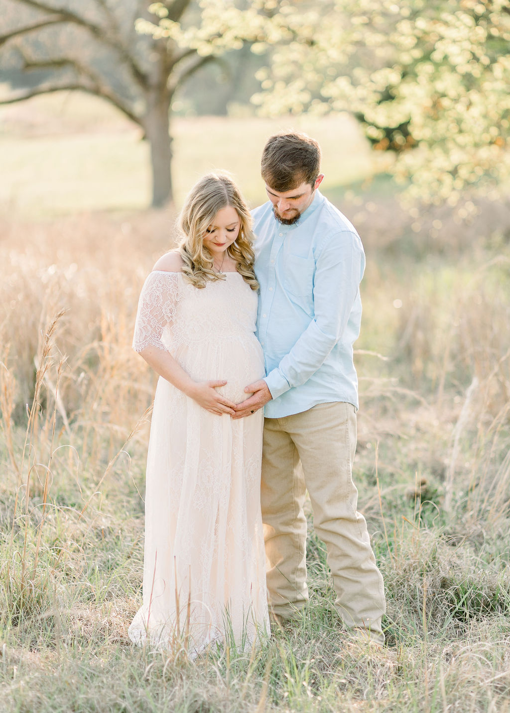 Mom and dad pose for maternity session in field while looking down at the belly. Image captured by Madison maternity photographer. 