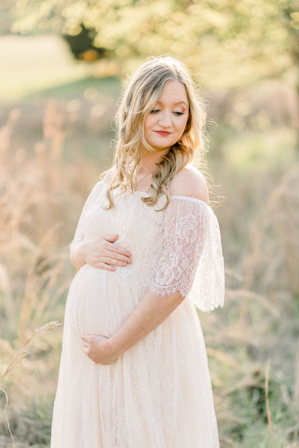 Mom wears white lace maxi dress in field with beautiful rim light lighting behind her. Image captured by CJ and Olive Photography, a Madison maternity photographer.