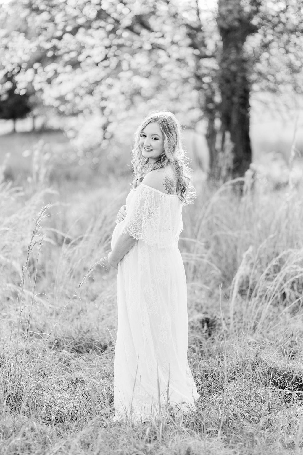 Mom wears white lace maxi dress in field with beautiful rim light lighting behind her. Black and white image captured by CJ and Olive Photography, a Madison maternity photographer.