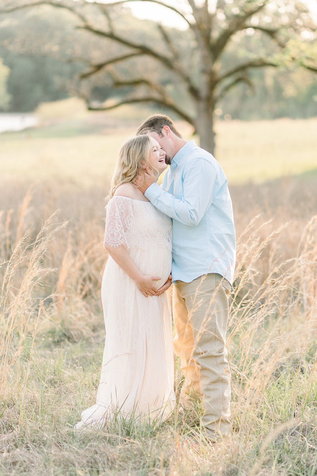 Mom in long white lace dress and dad  in light blue button up pose together for maternity session in a green field. Image taken by Madison maternity photographer, CJ and Olive Photography.