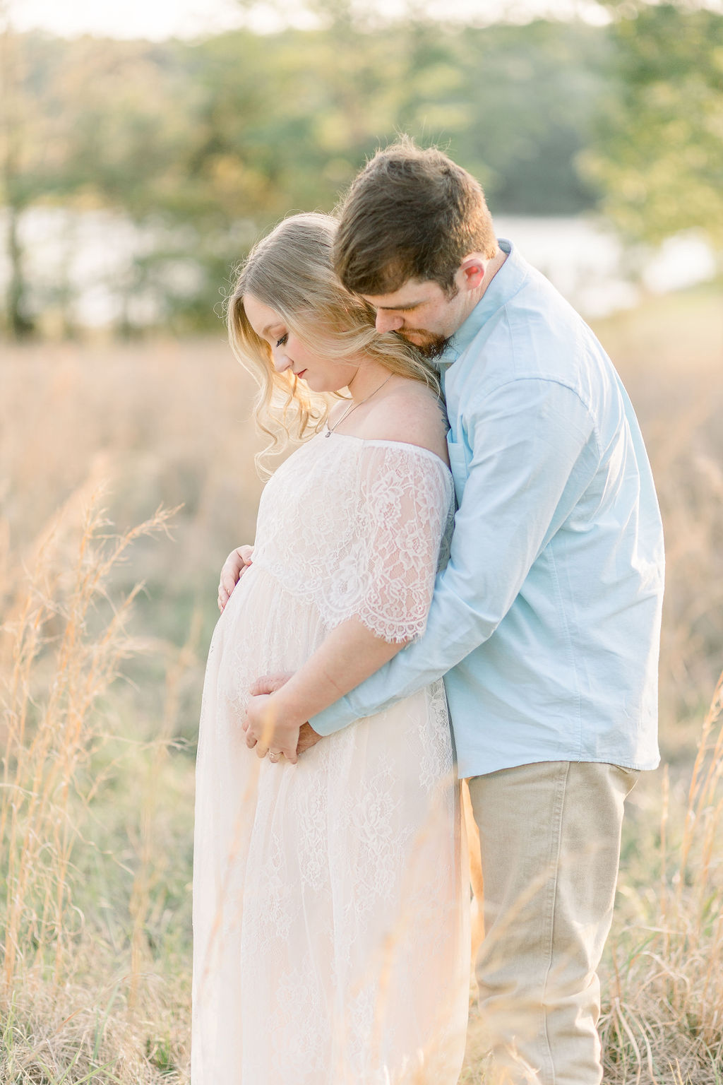 Mom and dad to be in green grassy field at sunset with dad behind mom and both hugging pregnant belly. Image captured by CJ and Olive Photography, a Madison Maternity Photographer. 