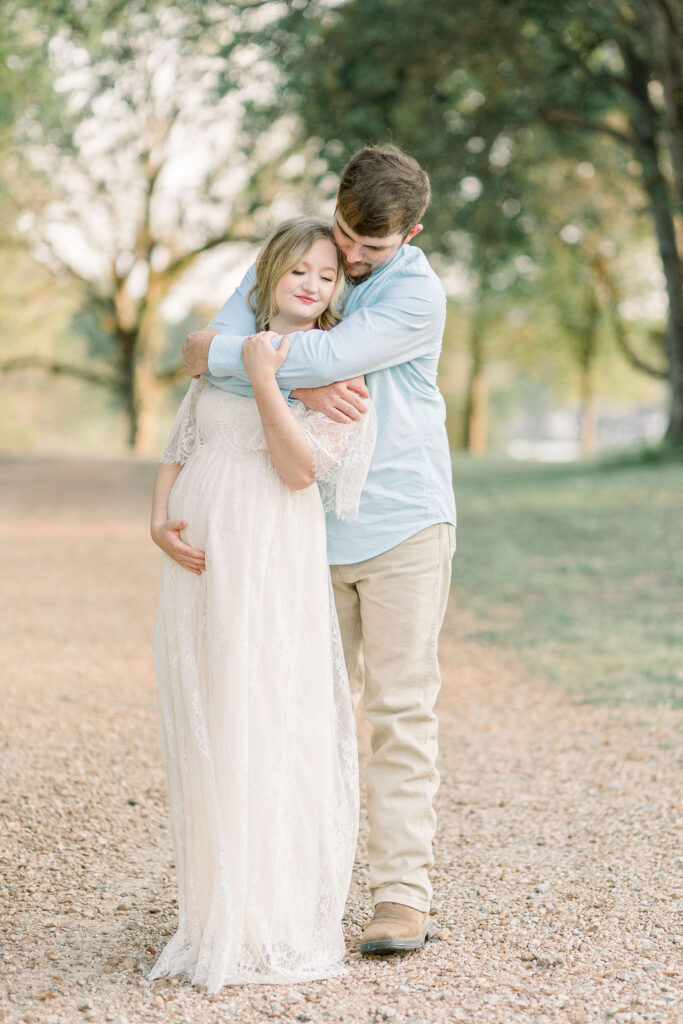 Mom and dad to be in green grassy field at sunset with dad behind mom and both hugging pregnant belly. Image captured by CJ and Olive Photography, a Madison Maternity Photographer. 