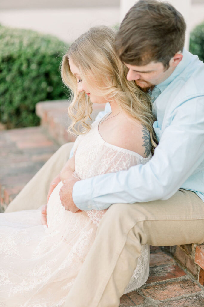 Mom and dad to be on red steps at sunset with dad behind mom and both hugging pregnant belly. Image captured by CJ and Olive Photography, a Madison Maternity Photographer. 