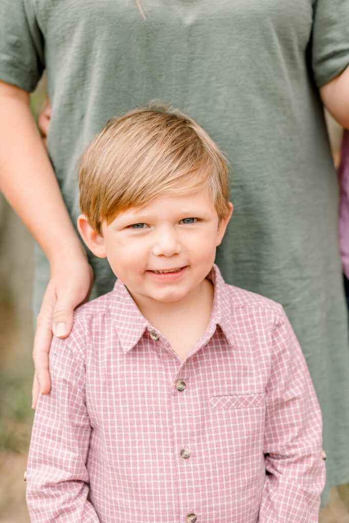 Little boy smiles at camera in a pink plaid button up shirt for fall photos. Image taken by Mississippi Family Photographer. 