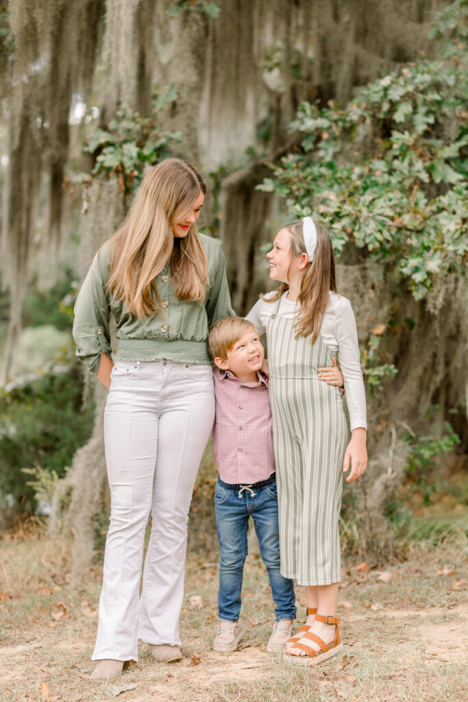 Mississippi family photographer captures image of three siblings standing together and smiling at each other for fall family photos. 