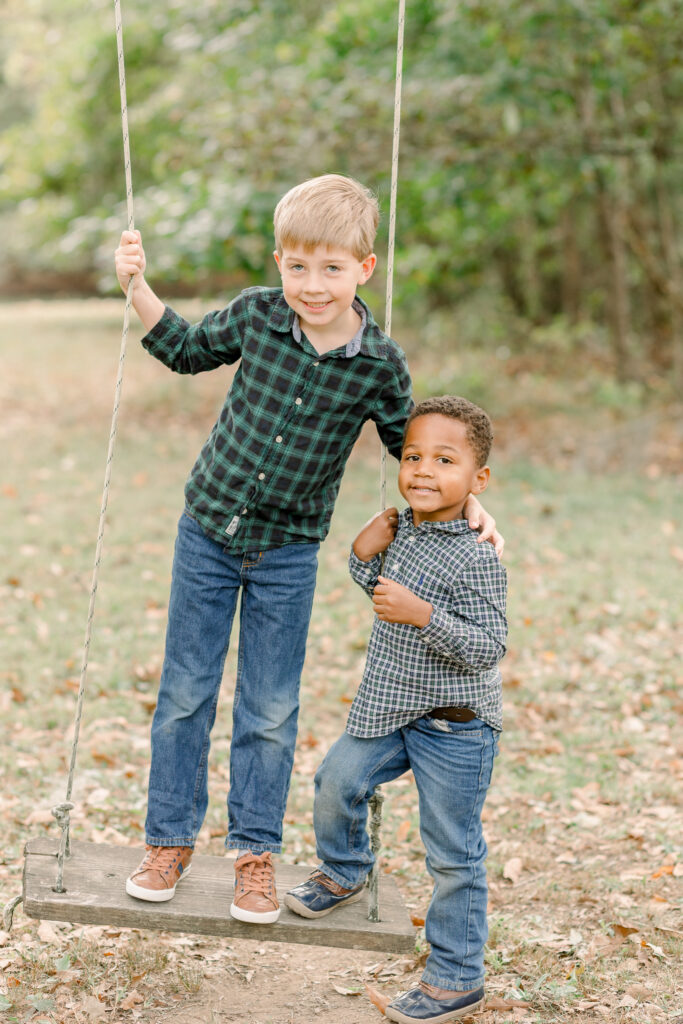 Two little boys smile at camera while on a tree swing for fall family photos. Image taken by CJ and Olive Photography. 