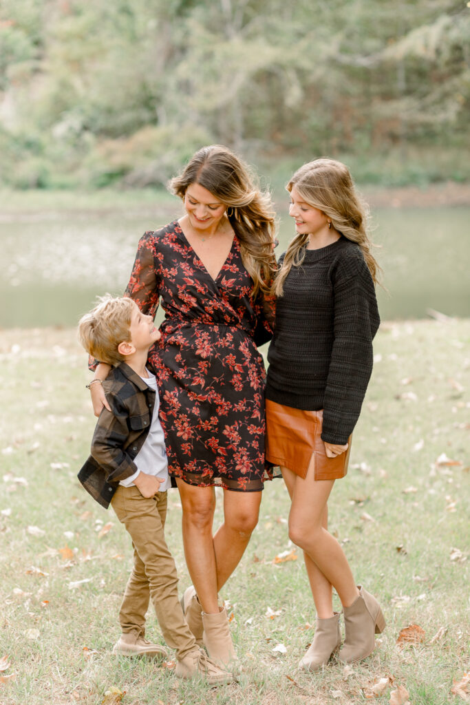 Mom with two kids smile at each other in front of pond for fall family photos at The Resting Place by CJ and Olive Photography. 