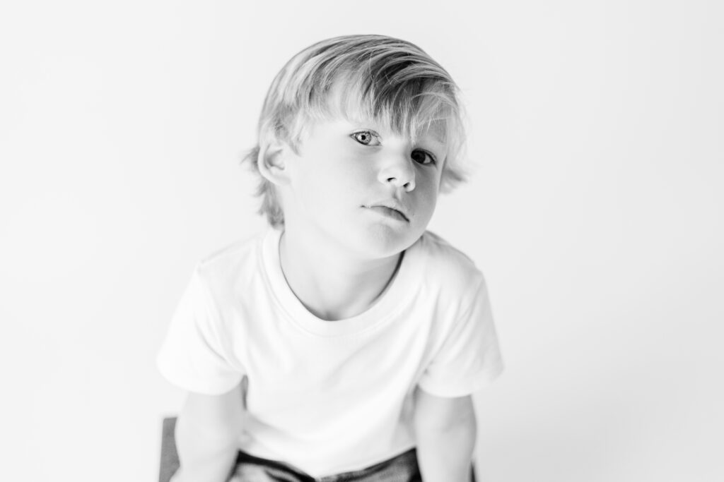 Black and white image of little boy giving a too cool look in white studio for personality portraits. Image captured by CJ and Olive Photography. 