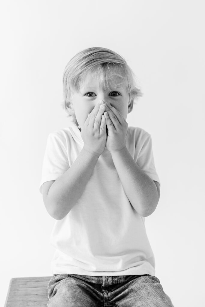 Black and white image taken by Brandon Family Photographer in white studio with little boy making a surprised face. 