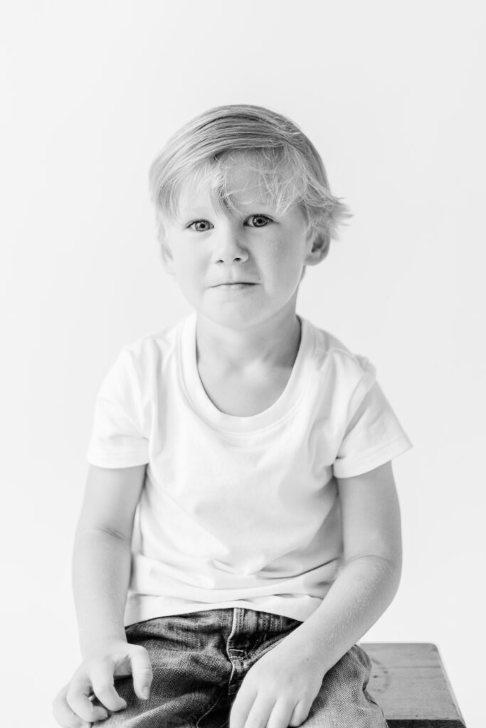 Black and white image taken by Brandon Family Photographer in white studio with little boy making a small grin. 